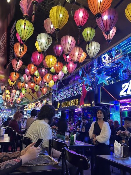 Interior of a vibrant bar in Hanoi's Old Quarter decorated with colorful lanterns, showcasing a lively atmosphere with patrons enjoying their drinks.