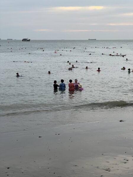 Busy beach in Vũng Tàu with locals swimming at sunset.