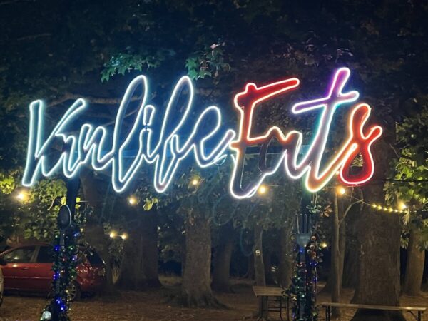 Neon Vanlife Eats” sign lit up at night, glowing under the trees